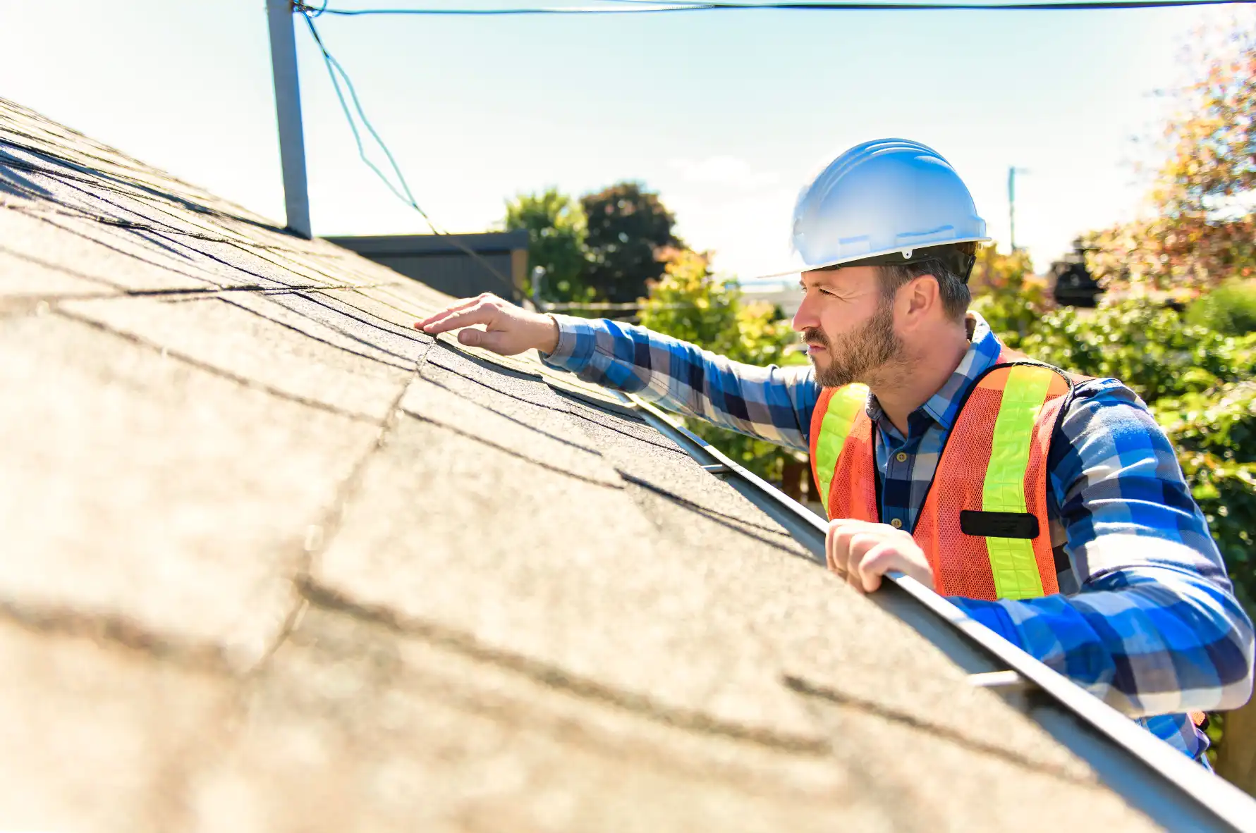 Inspector in a hard hat checking asphalt shingles on a roof