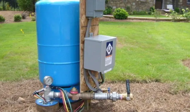 Well pressure tank, pressure switch and pump control box beside a house
